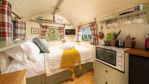 Een knus vertrek met een bed, een klein keukenblok en een raam met gordijnen.