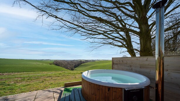 Een hottub in een houten omheining, met uitzicht op een groen veld en een boom.