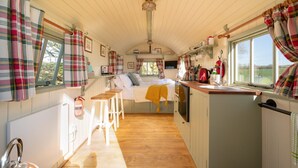 Een gezellig chaletinterieur met een bed, een klein keukenhoekje en een raam met uitzicht op een prachtig landschap.