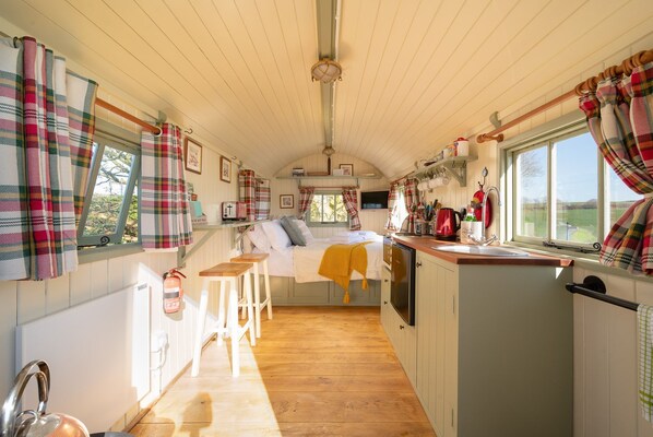 L’intérieur chaleureux d’un chalet comprend un lit, un petit coin cuisine et une fenêtre donnant sur un paysage pittoresque.
