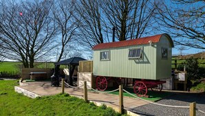 Een groene treinwagon met rode wielen, een klein wachtlokaal en een picknickplaats met een barbecue.