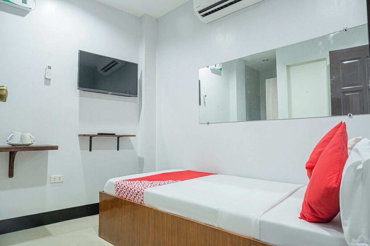 Una camera d'albergo con un letto, una televisione, uno specchio, un ripiano con tazze e una porta.