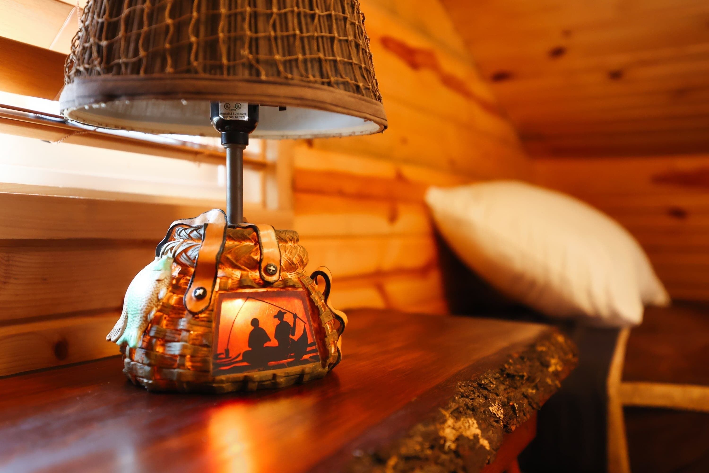 A lamp with a woven shade on a wooden table in a cabin.