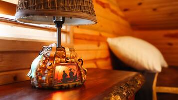 A lamp with a woven shade on a wooden table in a cabin.