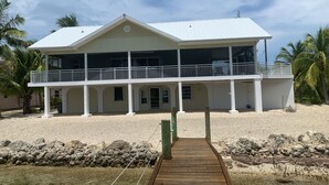 Ett tvåvåningshus vid stranden med en inglasad veranda och en träbrygga som leder ner till vattnet.