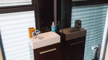 Ein modernes Badezimmer mit Duschkabine aus Glas, einem weißen Waschbecken mit Holzschrank und einer Toilette.
