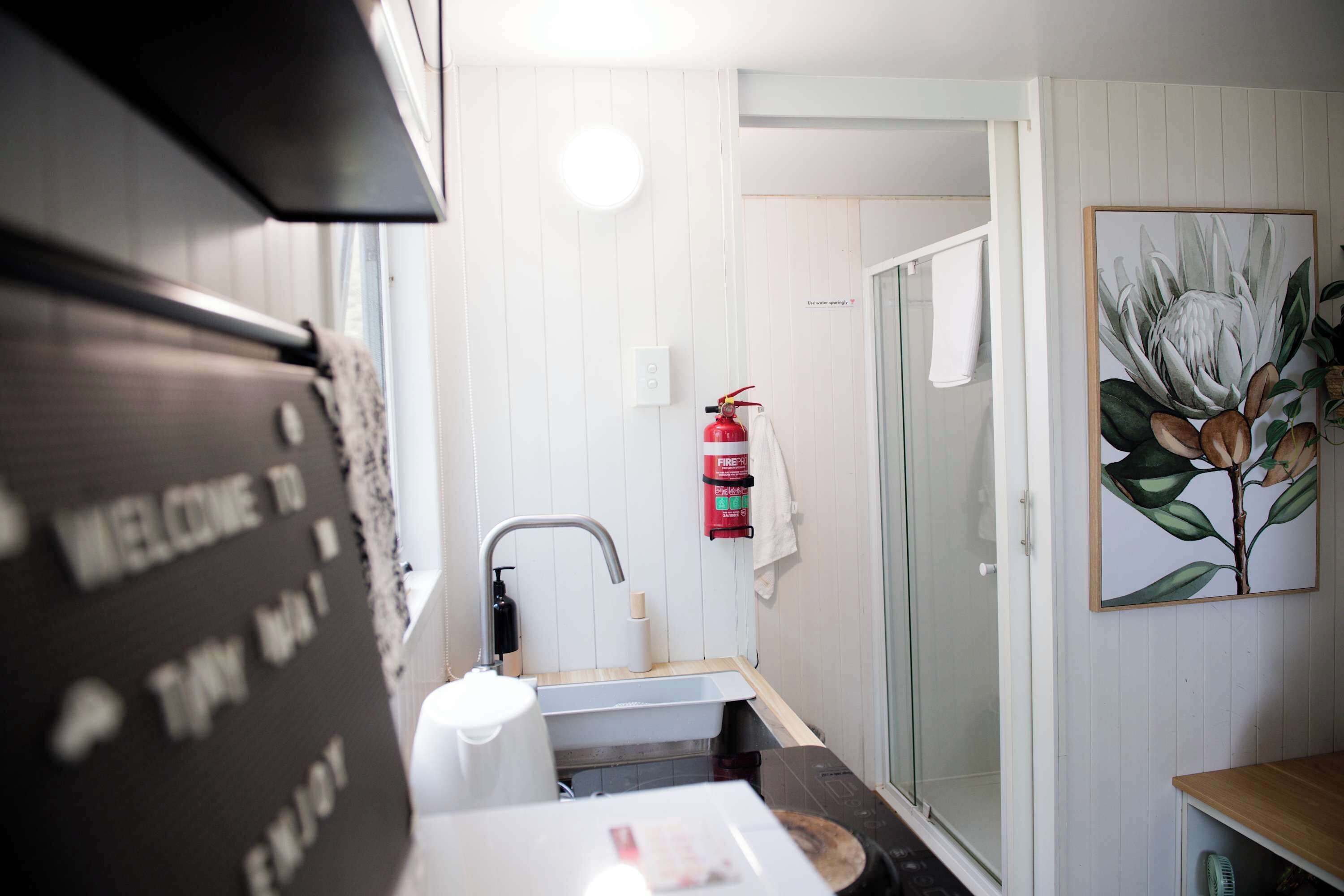 Un baño con lavamanos, toallero, extintor y cabina de ducha de cristal.