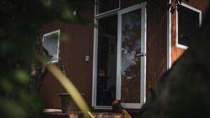 Une maison en bois avec une porte-fenêtre coulissante, une petite table avec une chaise et une plante en pot.