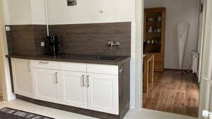 A kitchen with white cabinets, a dark wood backsplash, and a black coffee maker. - Quiet location, beautiful view, garden, charging station, table football, darts (Mellenbach Glasbach)