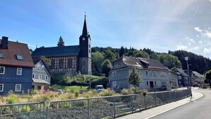 A historic town with traditional architecture, including a church with a clock tower and a stone building with timber framing. - Quiet location, beautiful view, garden, charging station, table football, darts (Mellenbach Glasbach)