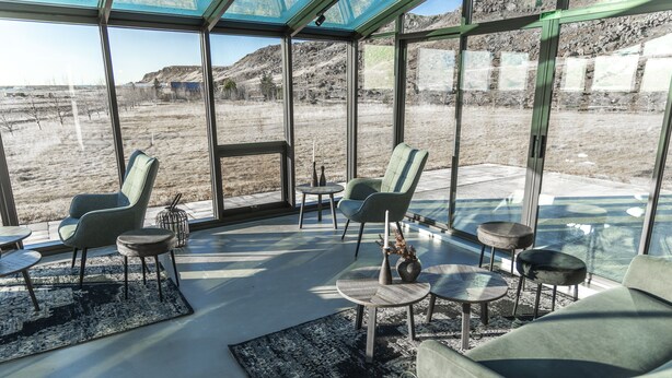 Un espace de vie moderne à aire ouverte, doté de grandes fenêtres, de sièges confortables et offrant une vue sur un paysage naturel.