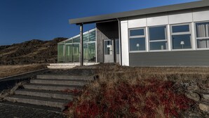 Un bâtiment moderne doté de grandes fenêtres et d’une porte en verre, situé sur une colline, sous un ciel dégagé.