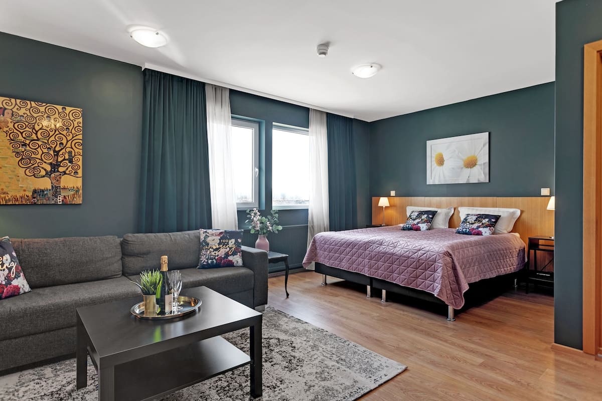 A modern bedroom with a bed, a sofa, a coffee table, and a painting on the wall.