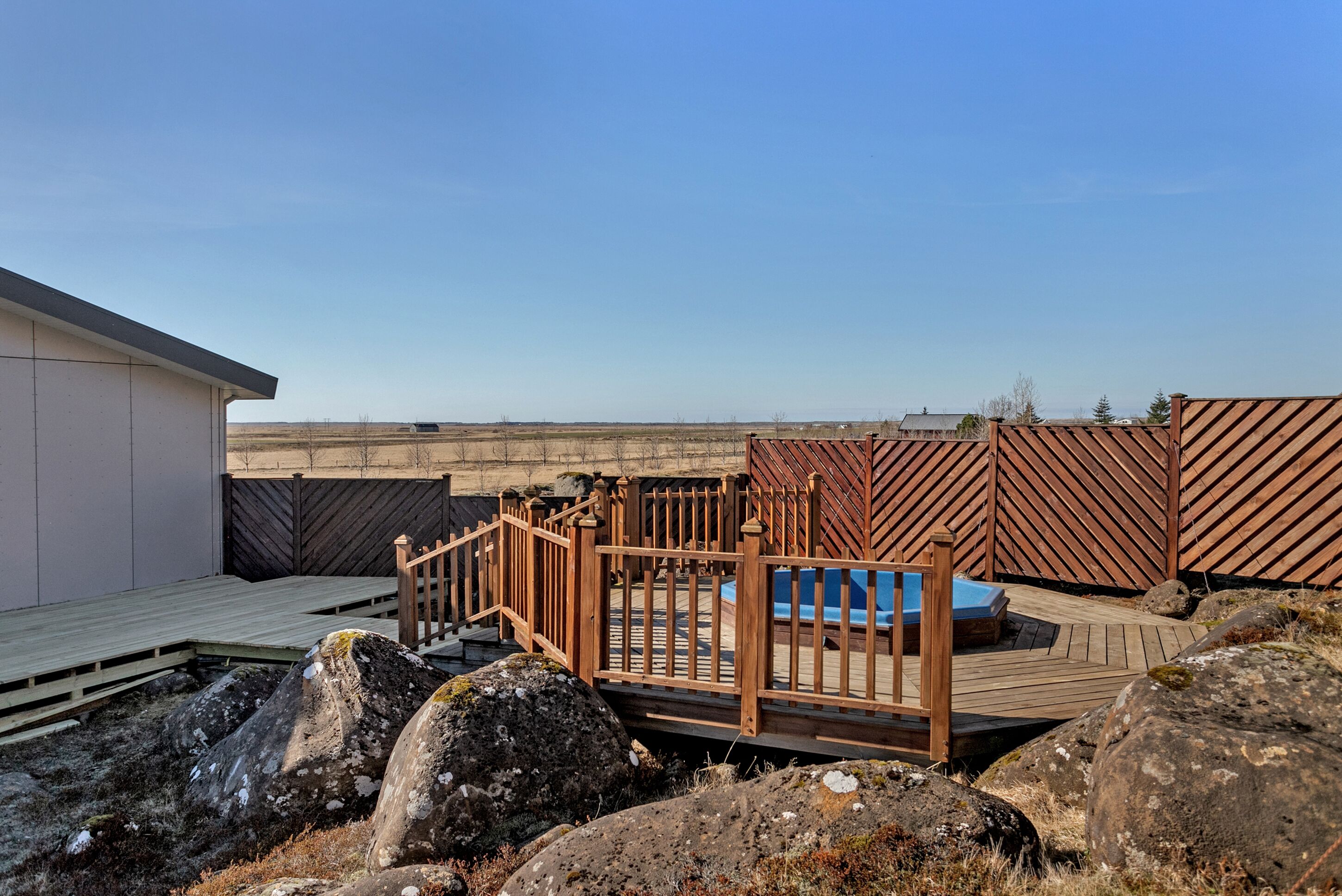 Eine Dachterrasse mit Holzzaun, kleinem Pool und großen Steinen.