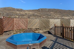 A blue hot tub on a wooden deck with a wooden fence and rocky hills in the background. - Hótel Kvika (Sveitarfélagid Ölfus)