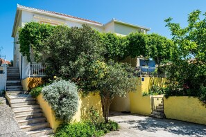 Stroll up to the charming building, surrounded by lush greenery and a small tree, and enjoy the view from the balcony with a metal railing.