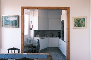 A compact kitchen with white cabinets, a coffee maker, and a kettle. There is a small dining area with a table and chairs. - Casa Didi - Sintra (Sintra)