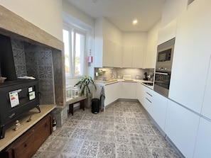 A modern kitchen with white cabinets, a built-in oven, and a microwave. There's a stone fireplace with a TV and a small plant on the counter. - Casa Didi - Sintra (Sintra)