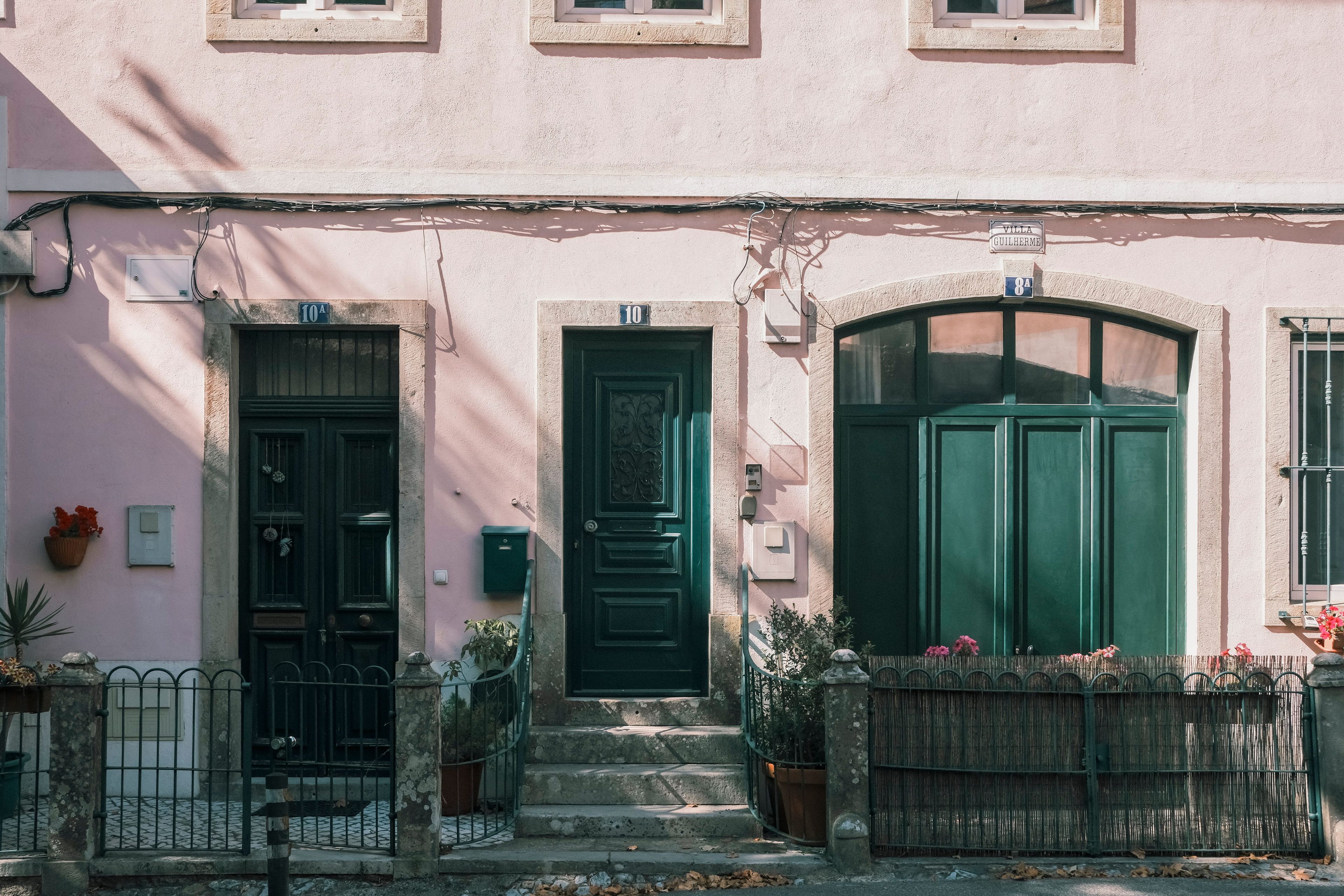 A pink building with three doors, a small porch, and a wooden fence.