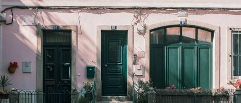 A pink building with three doors, a small porch, and a wooden fence.