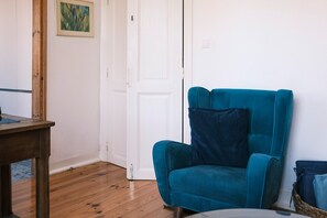 A room with a teal armchair, a wooden table, and a white door. - Casa Didi - Sintra (Sintra)