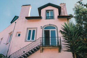 A pink building with a balcony, a staircase, and a window with a decorative grille. - Casa Didi - Sintra (Sintra)