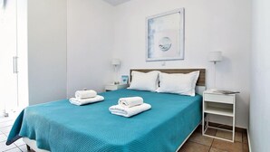 Una cama bien hecha con una colcha color turquesa, dos toallas blancas y un cabecero de madera.