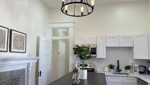 Een moderne keuken met witte kastjes, een donker houten eiland, een kroonluchter en een deur naar een andere kamer.