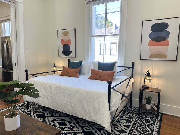 Een slaapkamer met een bed, kussens, een nachtkastje, een lamp en een plant.