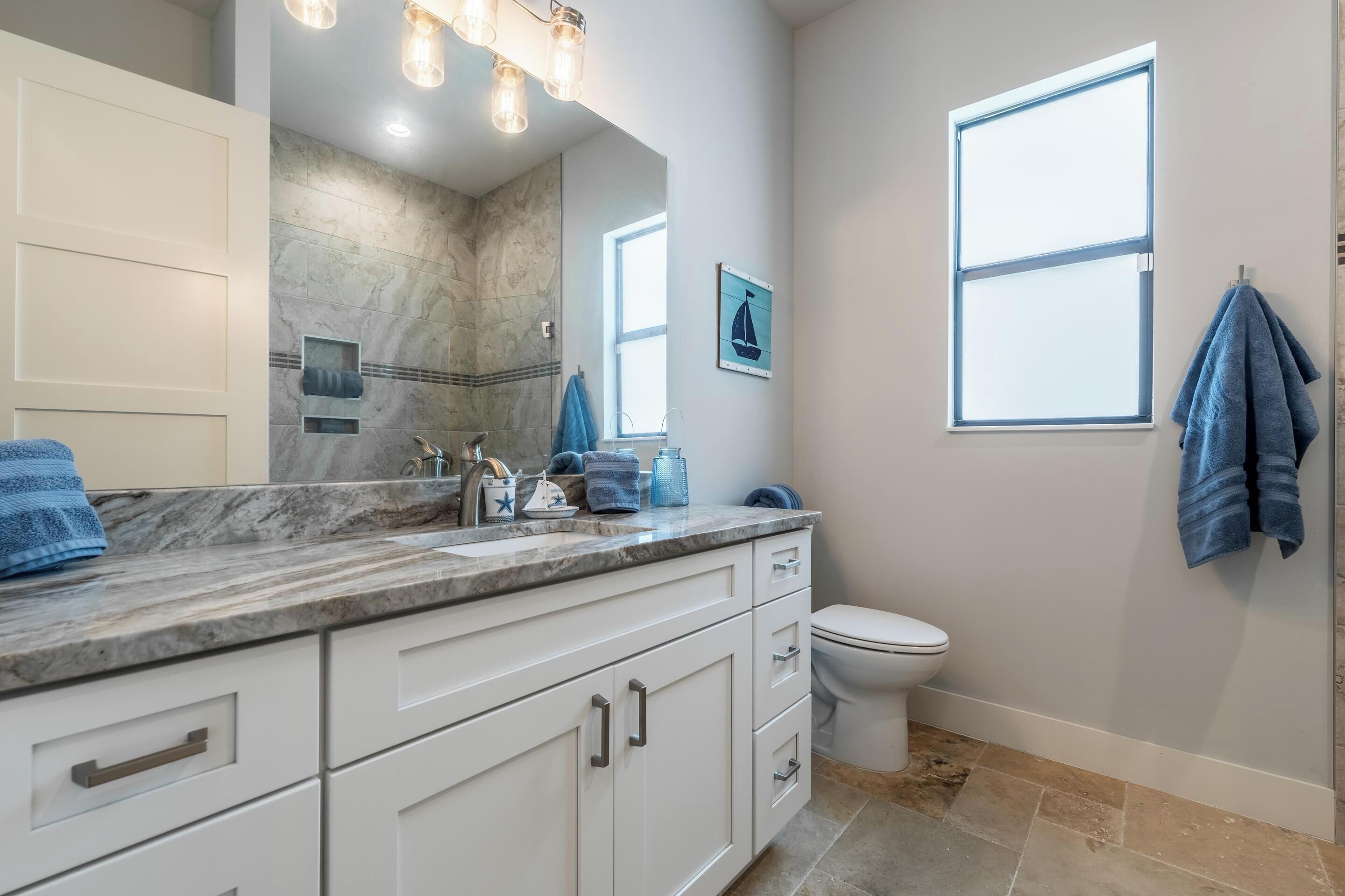 A bathroom with a marble countertop, a white toilet, a window, and a towel rack.