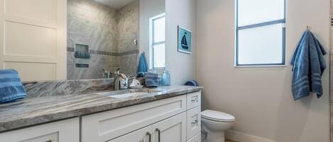 A bathroom with a marble countertop, a white toilet, a window, and a towel rack.