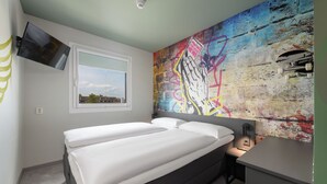 A modern bedroom with a large bed, a mounted TV, and a colorful graffiti wall. - Felix Hotel Darmstadt (Darmstadt)