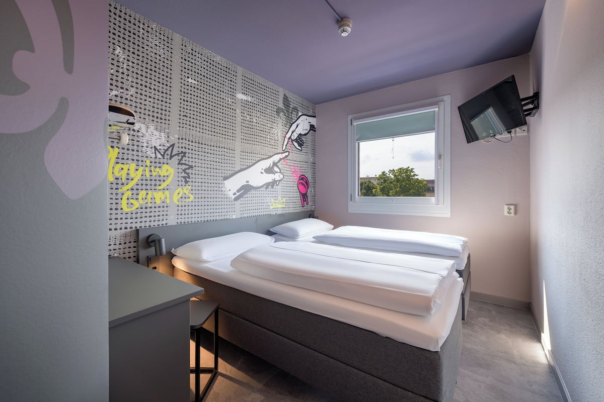 Un dormitorio moderno con una cama grande, un escritorio y un televisor instalado en la pared.