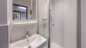 A modern bathroom with a glass-enclosed shower, a white sink, and a mirror above the sink. - Felix Hotel Darmstadt (Darmstadt)