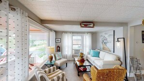 A living room with a sofa, chairs, a coffee table, and a lamp. There are windows with curtains, a wall-mounted picture, and a ceiling with a decorative pattern. - Room 8 (3rd Floor and Shared Bathroom) (Laconia)
