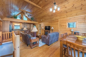 A wooden cabin interior with a dining area, sofas, a TV, and a kitchen. - Bearadise Mtn Cabin~Hot Tub+Fire Pit, Grill & WiFi (Burnsville)