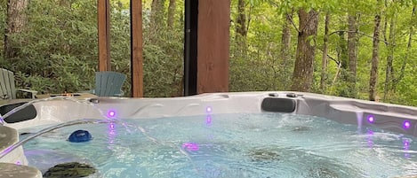 Ein Whirlpool mit Wasserstrahlen und LED-Beleuchtung, umgeben von einer Holzterrasse und Bäumen.