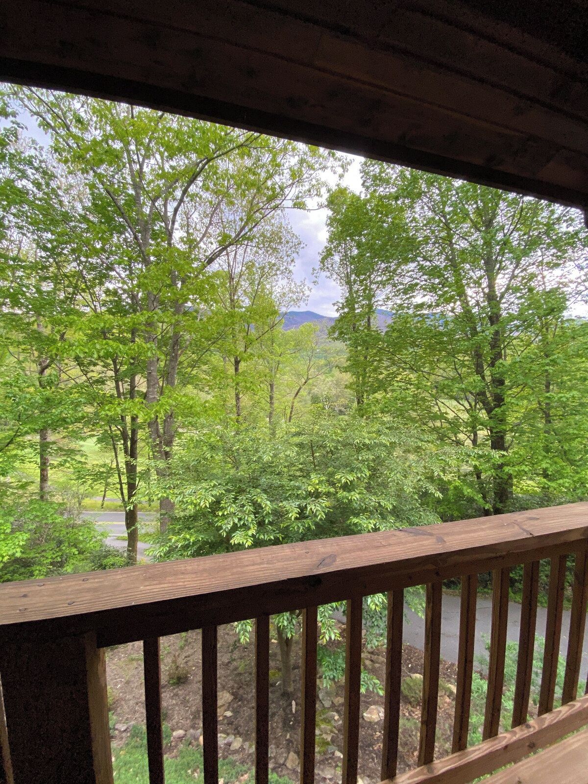 A wooden deck with a view of a forested area and a road.