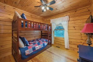 A bunk bed with a quilt, a ceiling fan, a window with curtains, and a lamp. - Bearadise Mtn Cabin~Hot Tub+Fire Pit, Grill & WiFi (Burnsville)