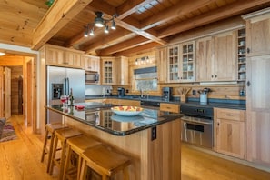 A kitchen with wooden cabinets, a central island with stools, stainless steel appliances, and a hanging light fixture. - Bearadise Mtn Cabin~Hot Tub+Fire Pit, Grill & WiFi (Burnsville)