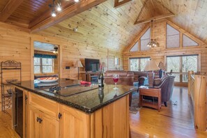 A wooden cabin interior with a kitchen island, dining table, and seating area.
