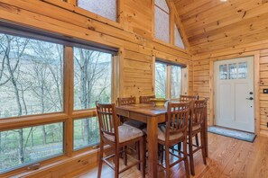 A wooden cabin interior with a dining table and chairs, large windows, and a door. - Bearadise Mtn Cabin~Hot Tub+Fire Pit, Grill & WiFi (Burnsville)