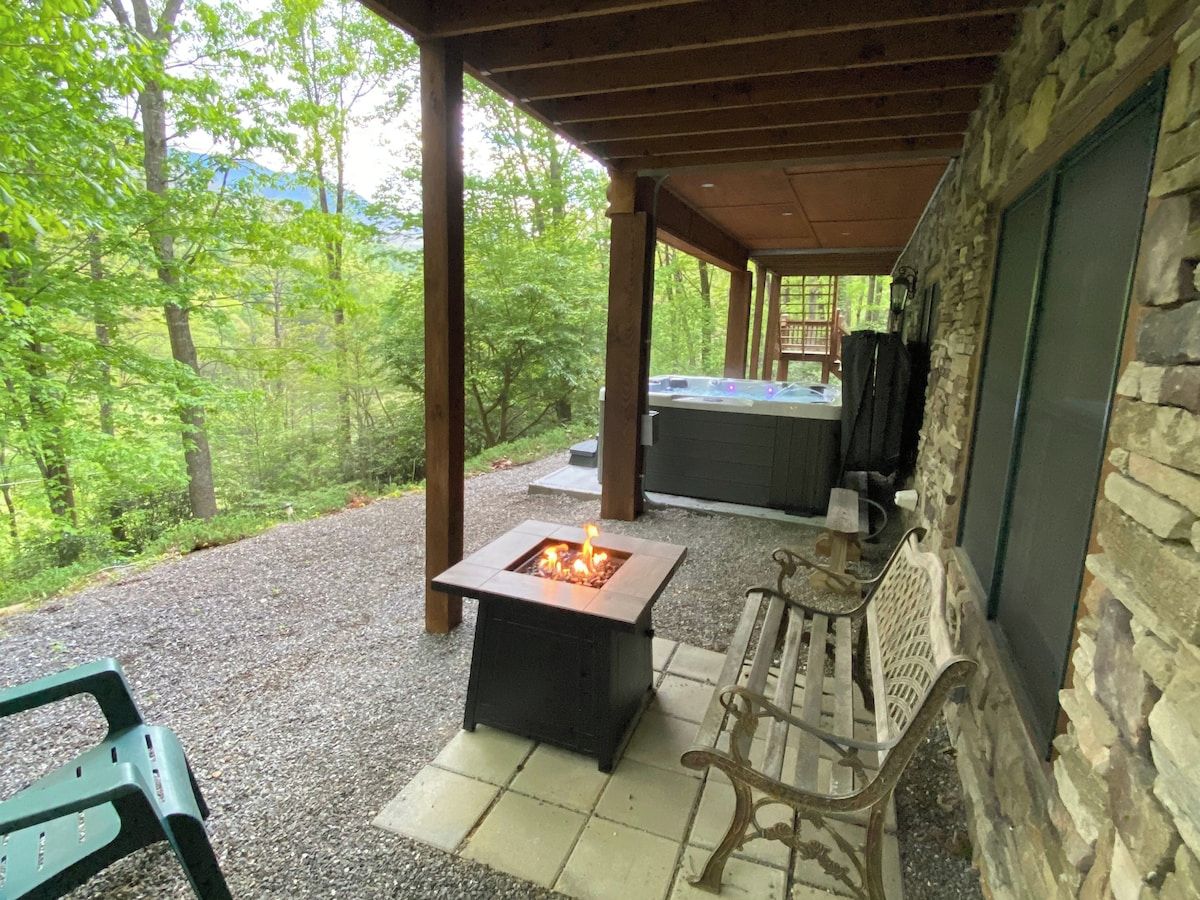 An outdoor patio with a square fire pit, seating, and a stone wall.