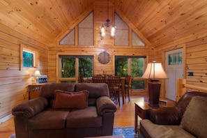 A wooden cabin interior with a dining area, a sofa, and a lamp.