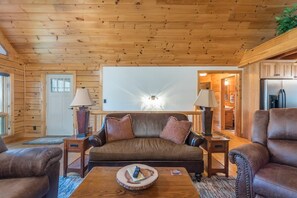 A cozy cabin interior with a wooden ceiling, a brown leather sofa, a wooden coffee table, and a refrigerator. - Bearadise Mtn Cabin~Hot Tub+Fire Pit, Grill & WiFi (Burnsville)