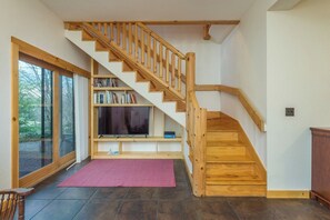 A staircase with wooden railings leading to a landing with a flat-screen TV and bookshelves.