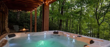 Ein Whirlpool mit Holzterrasse und Lichterketten, umgeben von Bäumen.