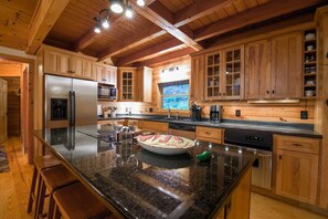 A kitchen with wooden cabinets, a stainless steel refrigerator, a microwave, and a large island with a bowl of food.