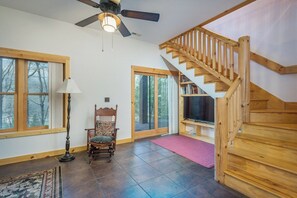 A spacious room with a wooden staircase, a large window, a chair, and a floor lamp.