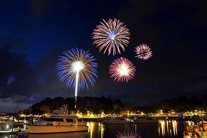 Een jachthaven 's nachts met afgemeerde boten en vuurwerk aan de hemel.